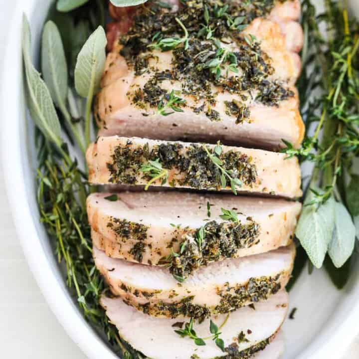 Top down view of a roasted turkey breast sliced thick and garnished with fresh herbs.