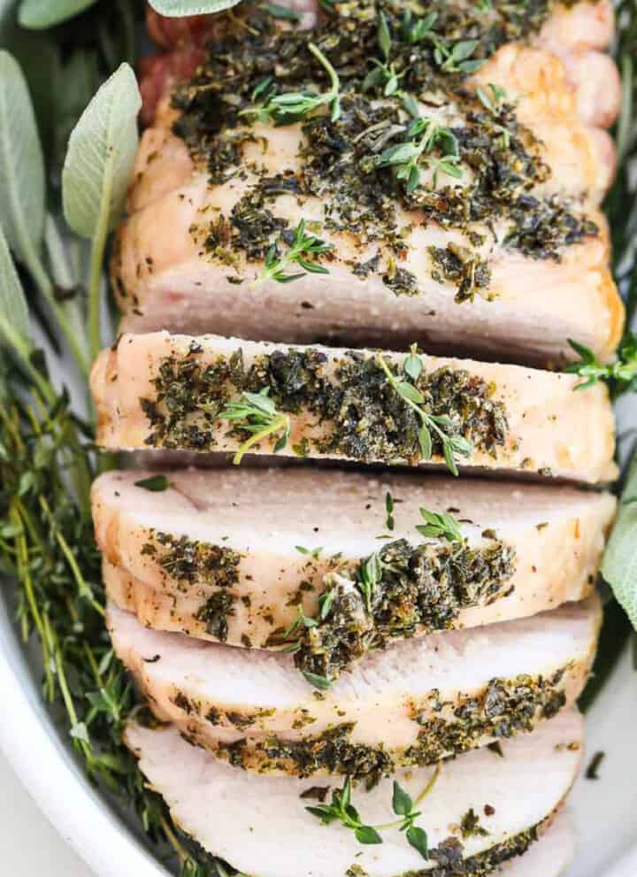 Top down view of a roasted turkey breast sliced thick and garnished with fresh herbs.