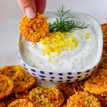 A lady dipping a zucchini chip into a lemon dill yogurt dip.