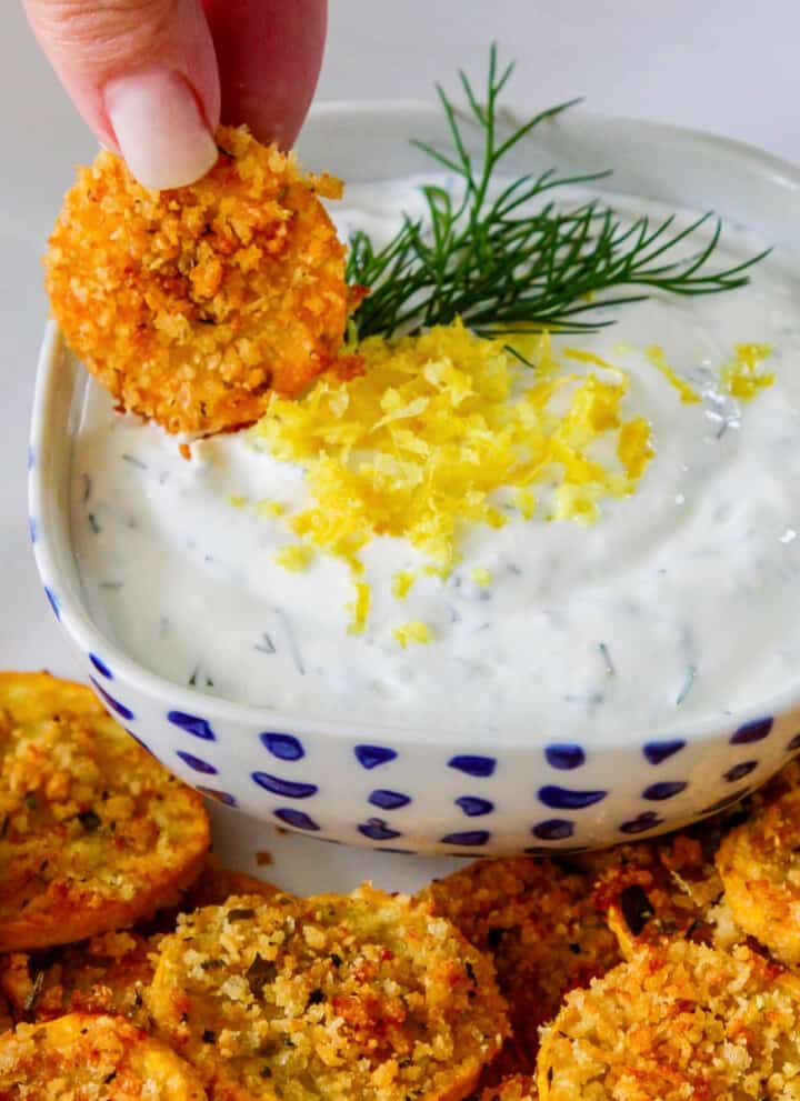 A lady dipping a zucchini chip into a lemon dill yogurt dip.