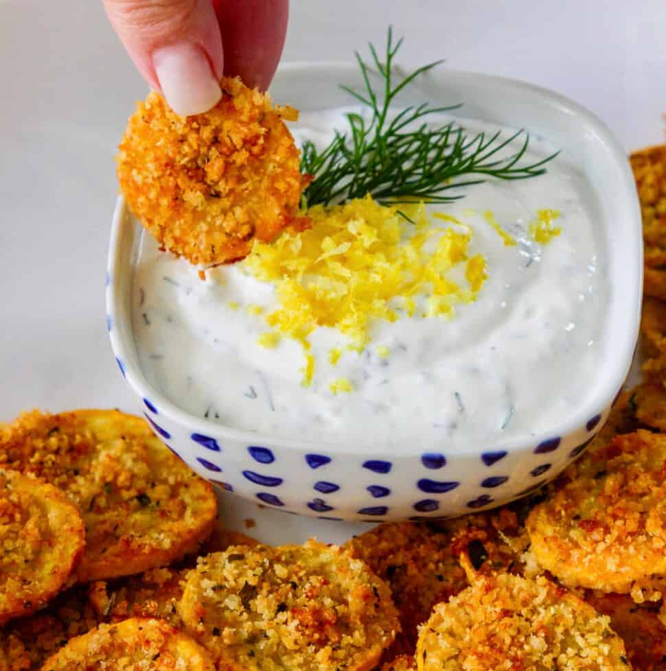 A lady dipping a zucchini chip into a lemon dill yogurt dip.