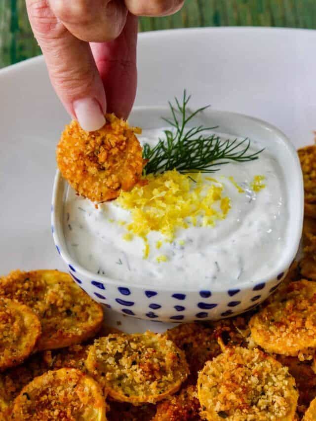 A lady dipping a crisp zucchini chip into yogurt dip.