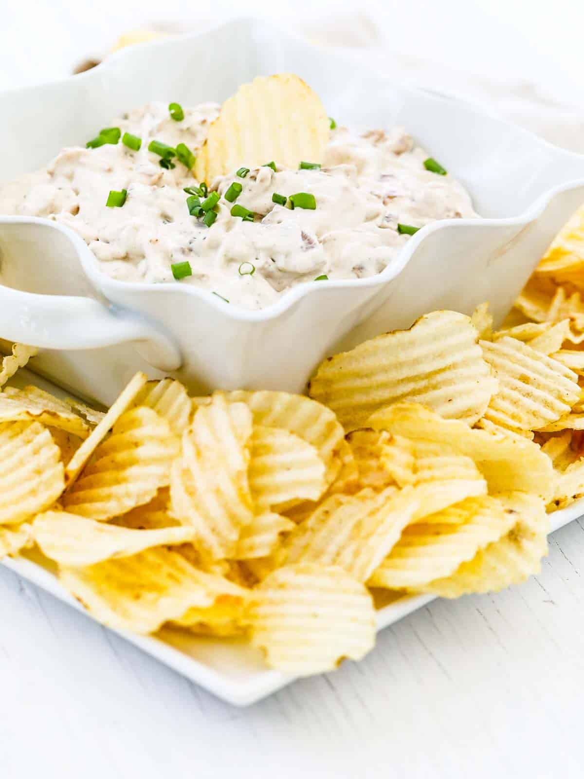 A white dish with curved edge with onion dip and a ruffled potato chip stuck inside.