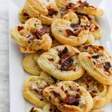 A white platter filled with brie and bacon palmier appetizers golden brown and ready to eat.