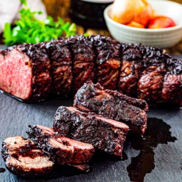 Thick sliced roast beef on a cutting board with pan juices and ingredients in the background.