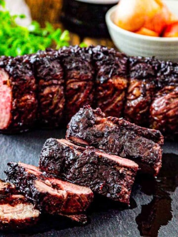 Thick sliced roast beef on a cutting board with pan juices and ingredients in the background.