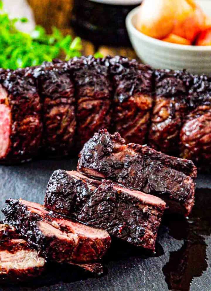 Thick sliced roast beef on a cutting board with pan juices and ingredients in the background.