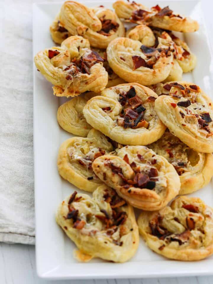 A white platter filled with brie and bacon palmier appetizers golden brown and ready to eat.