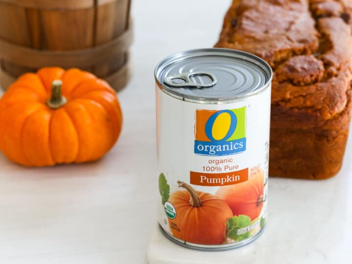 A can of canned pumpkin next to a loaf of baked pumpkin bread and a small pumpkin.