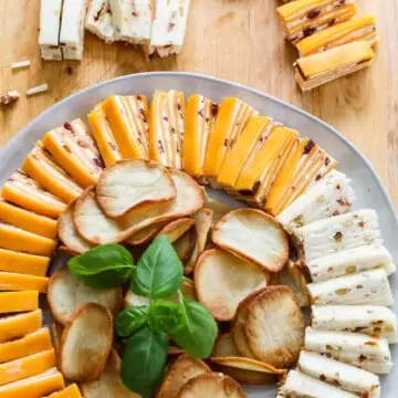 White round plate filled with cheese appetizers with crackers and garnished with basil.