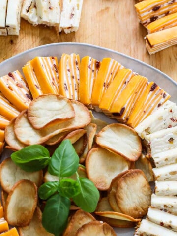 White round plate filled with cheese appetizers with crackers and garnished with basil.