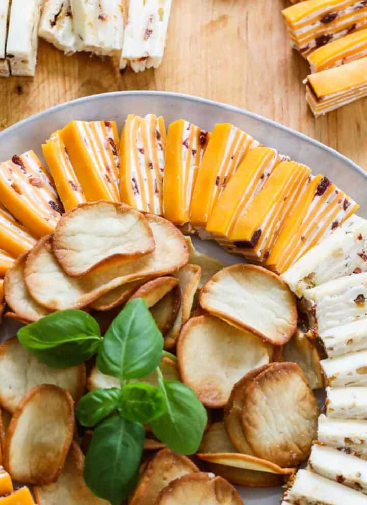 White round plate filled with cheese appetizers with crackers and garnished with basil.