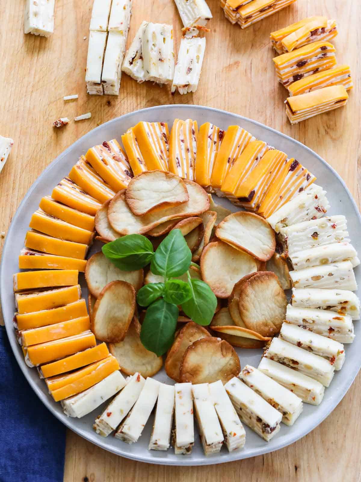 White round plate filled with finger food cheese appetizers with crackers and garnished with basil.