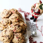 A white rectangle plate filled with chocolate chip peppermint cookies with a small Santa nearby.