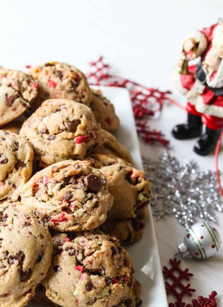 A white rectangle plate filled with chocolate chip peppermint cookies with a small Santa nearby.