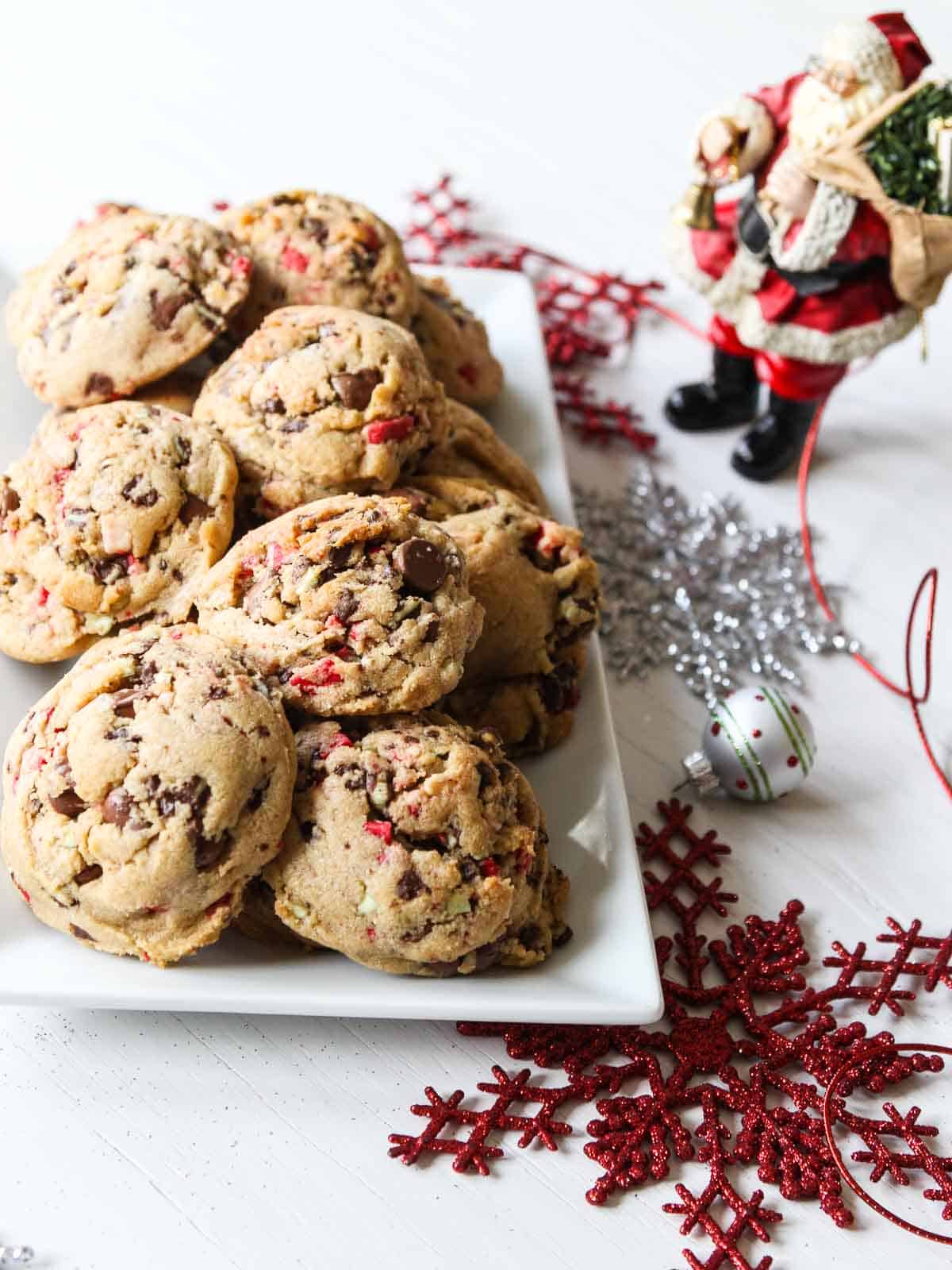 A white rectangle plate filled with chocolate chip peppermint cookies with a small Santa nearby.