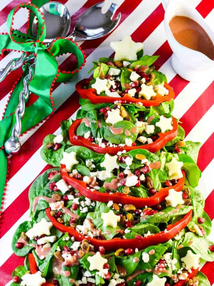 A salad shaped like a christmas tree with garland and ornaments made from fruit, nuts, and red bell pepper.