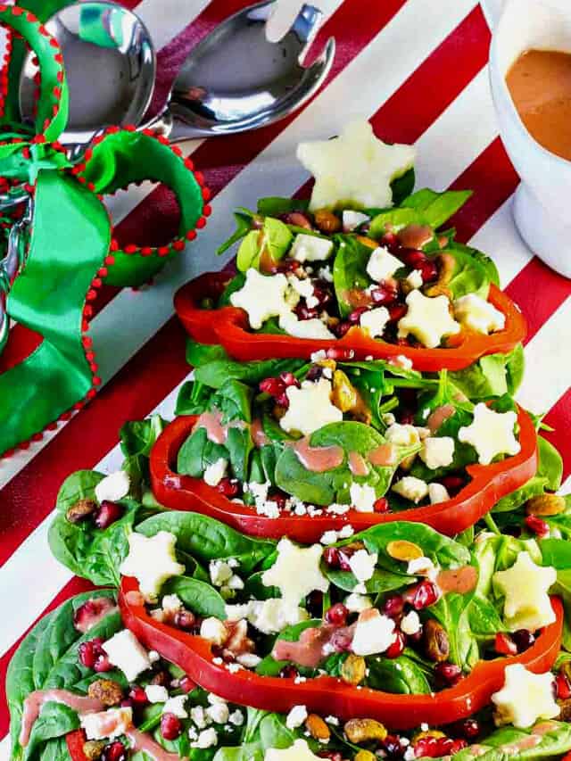 A salad shaped like a Christmas tree with red bell pepper garland, white apple stars and ornaments of nuts and fruit.