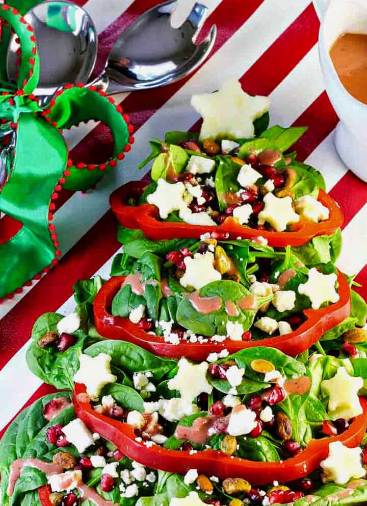 A salad shaped like a Christmas tree with red bell pepper garland, white apple stars and ornaments of nuts and fruit.