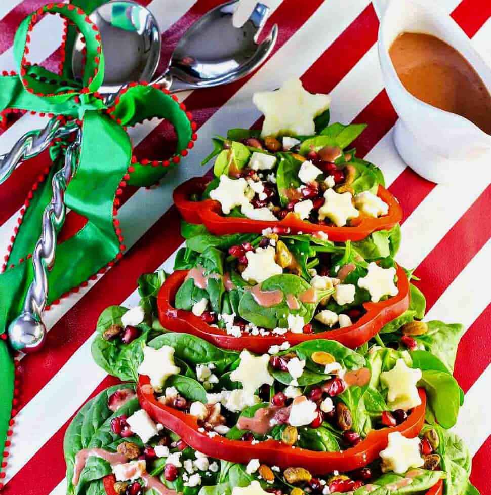 A salad shaped like a Christmas tree with red bell pepper garland, white apple stars and ornaments of nuts and fruit.