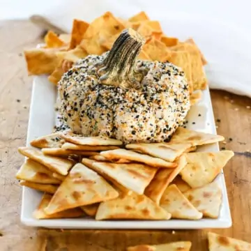 A pumpkin shaped cheese ball on a platter with pita chips and crackers.