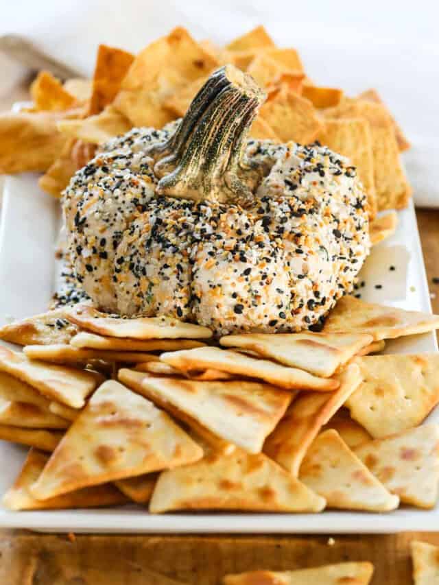 A pumpkin shaped cheese ball on a platter with pita chips and crackers.