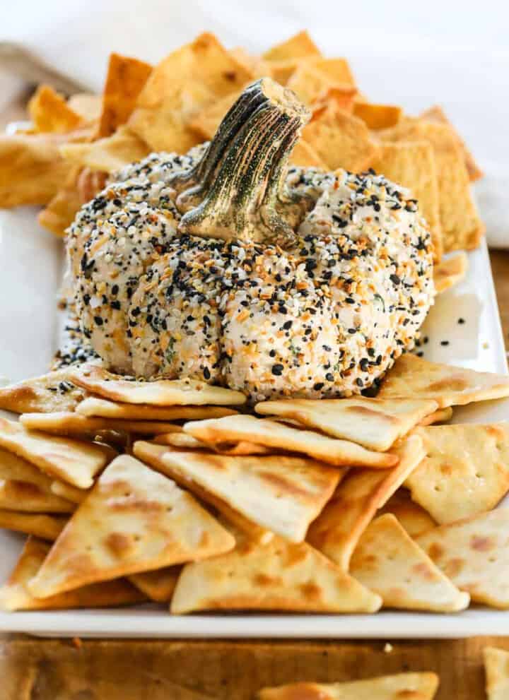 A pumpkin shaped cheese ball on a platter with pita chips and crackers.