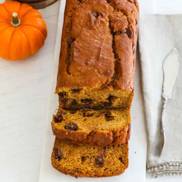 A baked loaf of pumpkin bread sliced thick with a silver knife.s