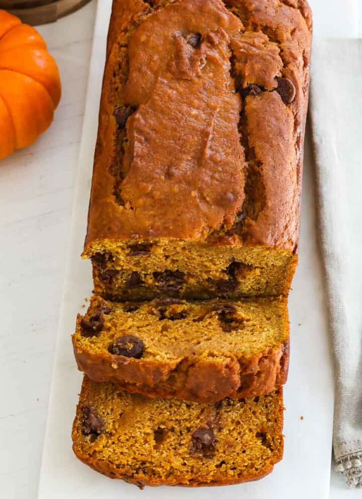 A baked loaf of pumpkin bread sliced thick with a silver knife.s