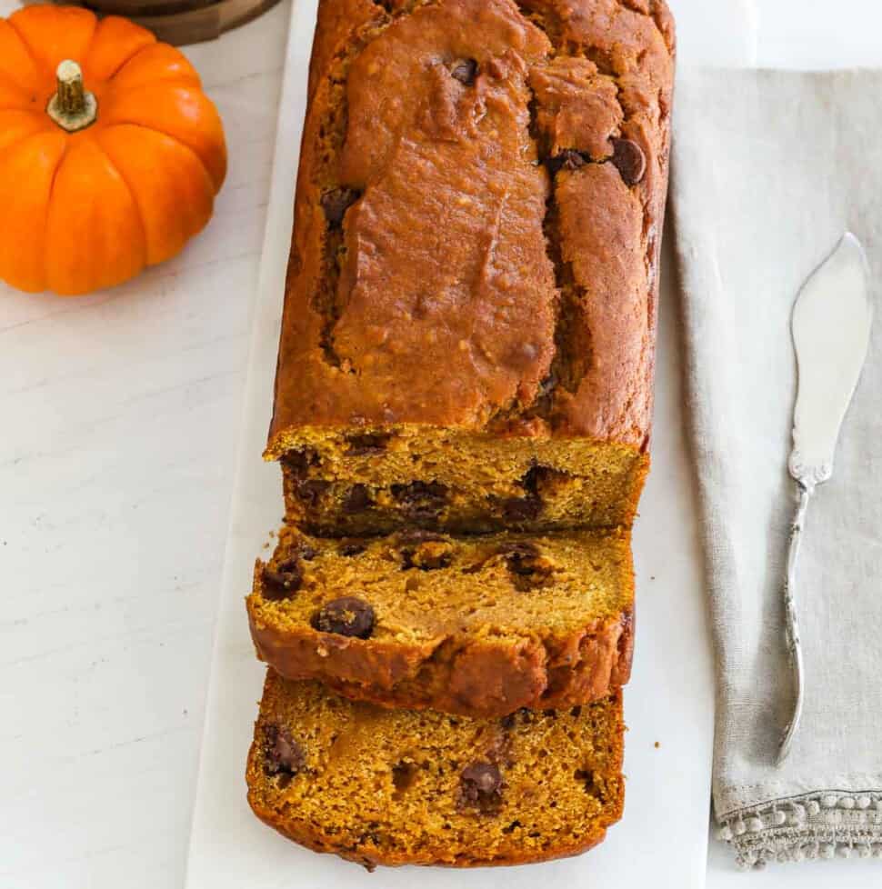 A baked loaf of pumpkin bread sliced thick with a silver knife.s