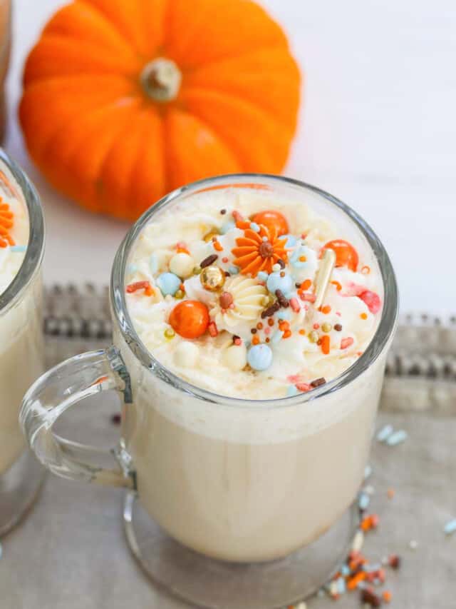 A glass mug filled with Pumpkin Spice Latte with whip cream and sprinkles.