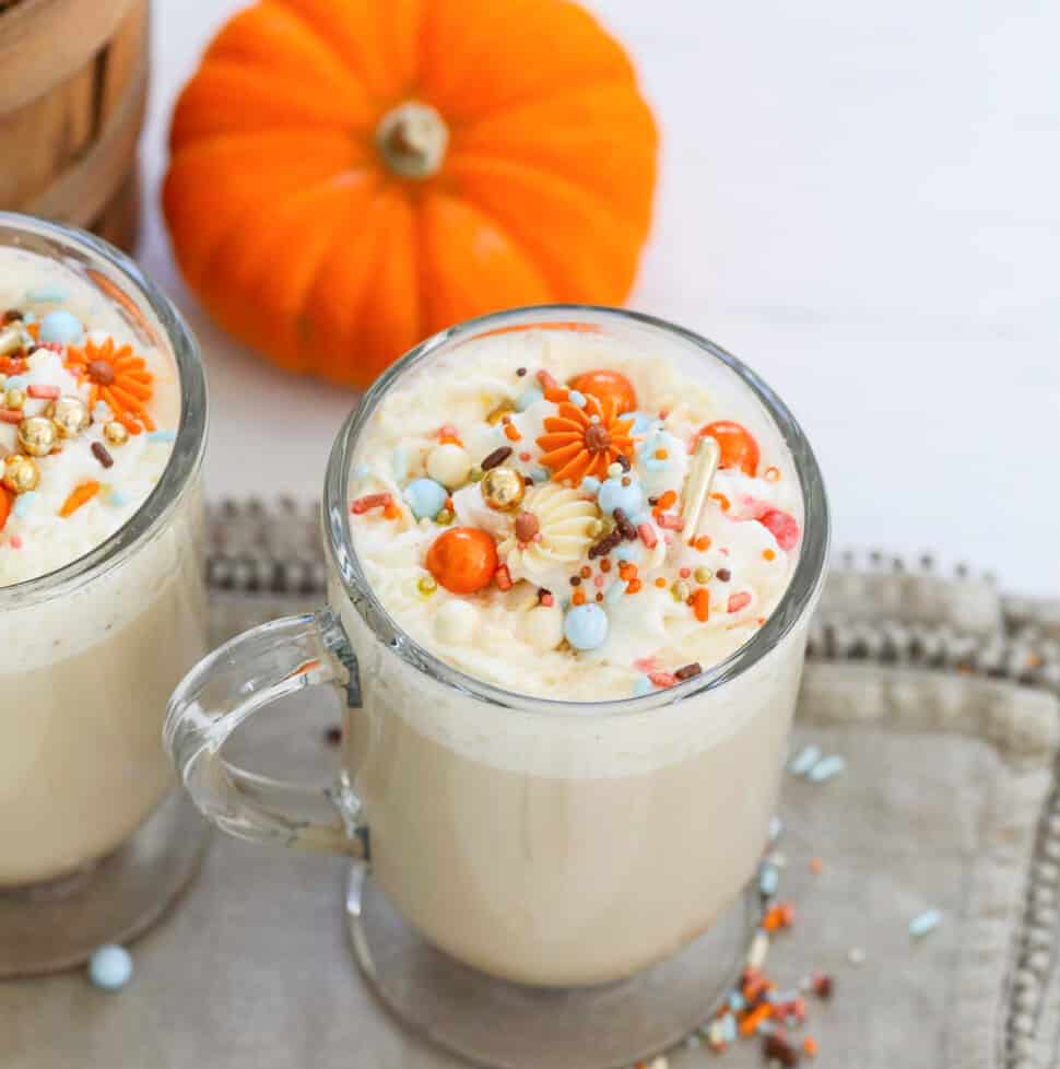 A glass mug filled with Pumpkin Spice Latte with whip cream and sprinkles.