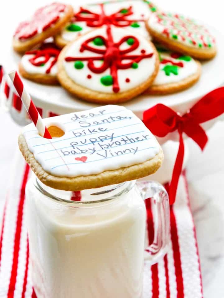 A glass of cold milk with a Christmas cookie on top with child wish list on top.