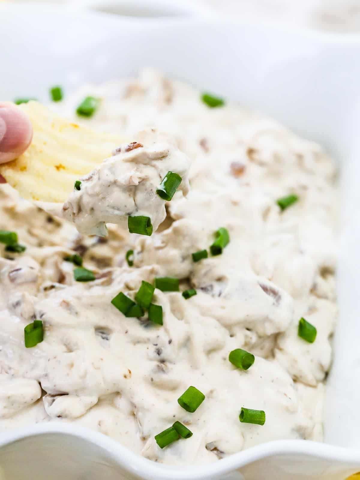 A person scooping French onion dip out of bowl with a ruffled potato chips