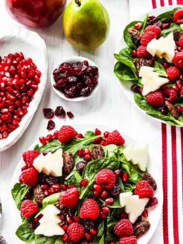 Two plates of Christmas salad with forks topped with fruit and nuts.