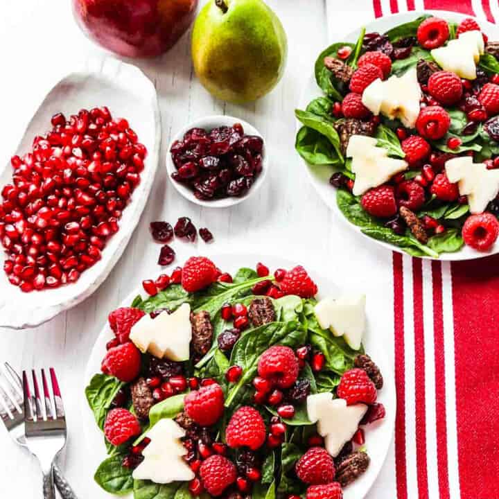 Two plates of Christmas salad with forks topped with fruit and nuts.