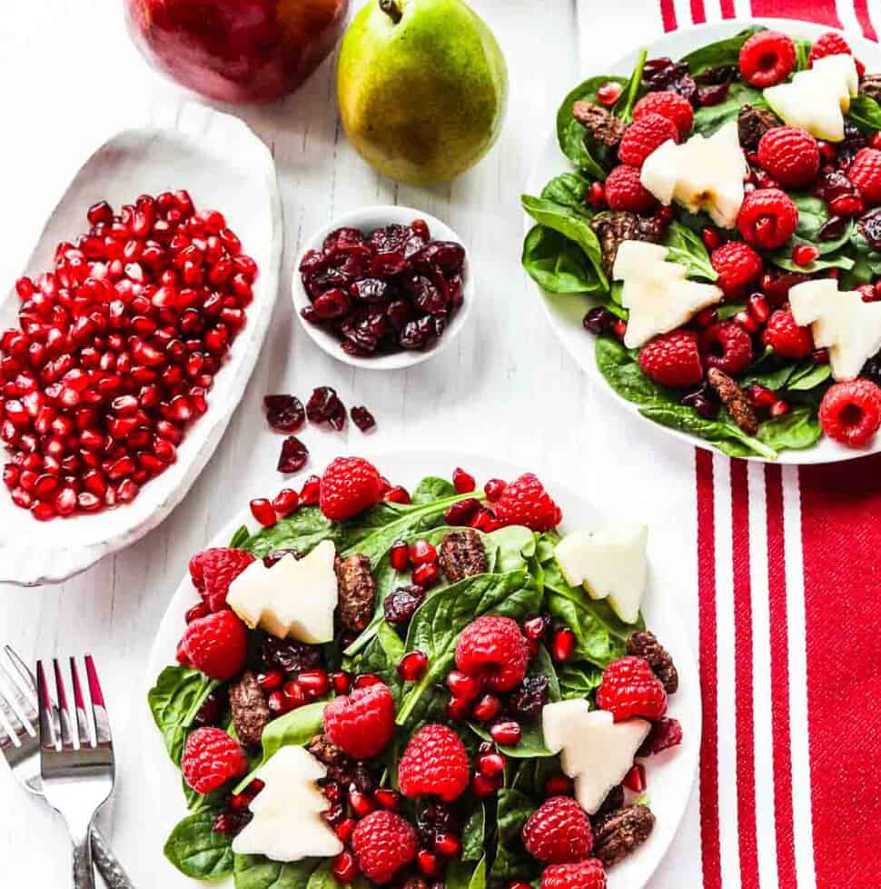 Two plates of Christmas salad with forks topped with fruit and nuts.