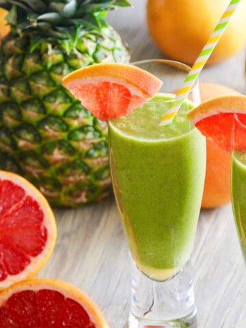 Two glasses of a green smoothie recipe garnished with grapefruit slices and straws.