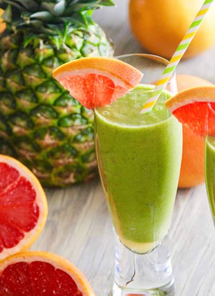 Two glasses of a green smoothie recipe garnished with grapefruit slices and straws.