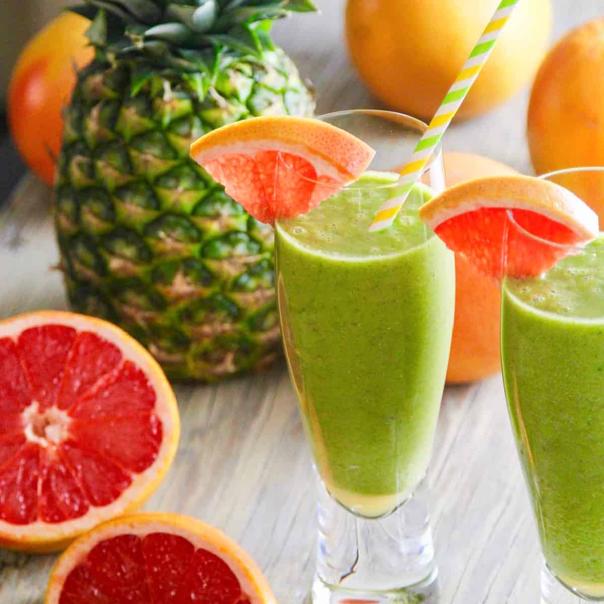 Two glasses of a green smoothie recipe garnished with grapefruit slices and straws.