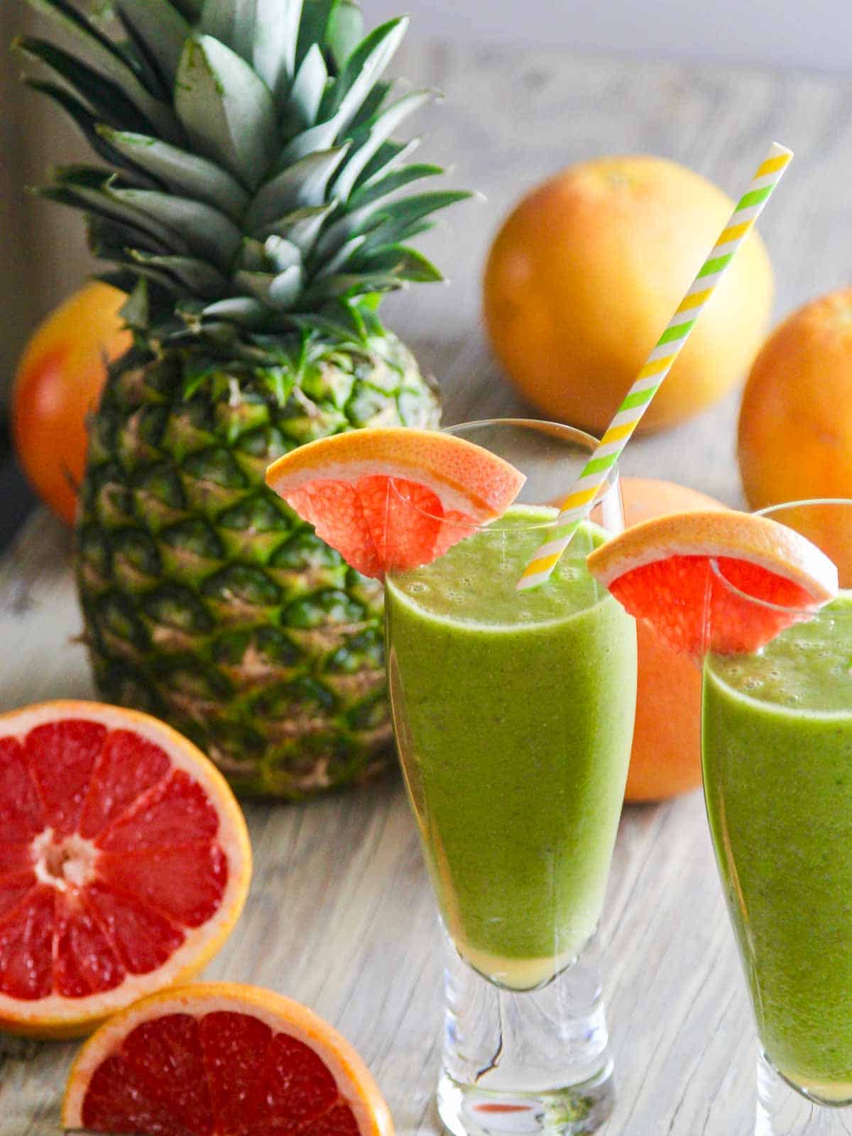 Two glasses of a green smoothie recipe garnished with grapefruit slices and straws.