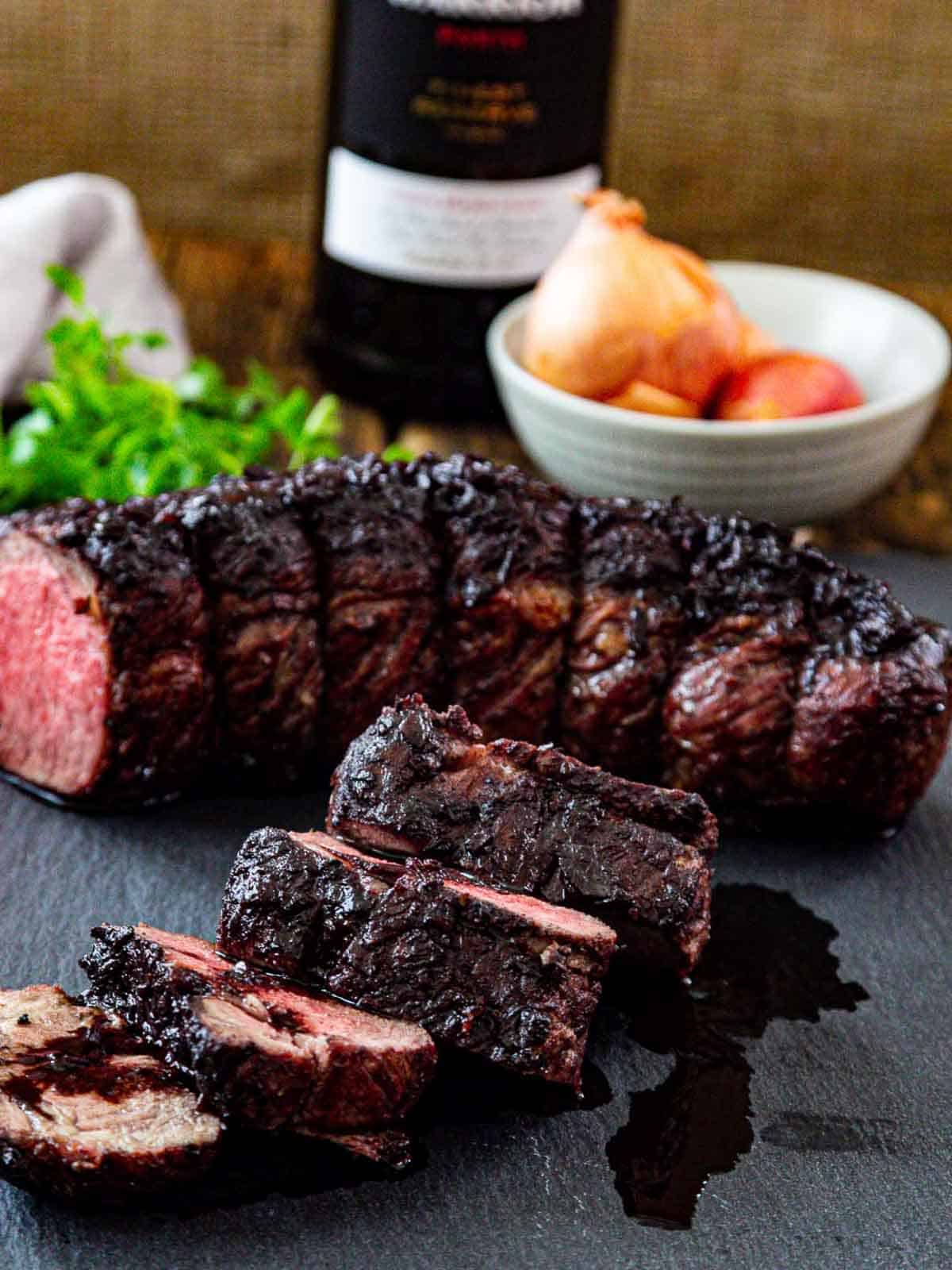 Thick sliced roast beef made with a rich wine sauce sliced on a board.