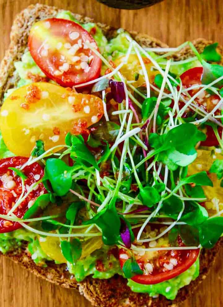 A close up photo of a slice of avocado toast topped with small heirloom tomatoes and microgreens.