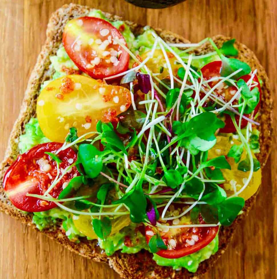 A close up photo of a slice of avocado toast topped with small heirloom tomatoes and microgreens.