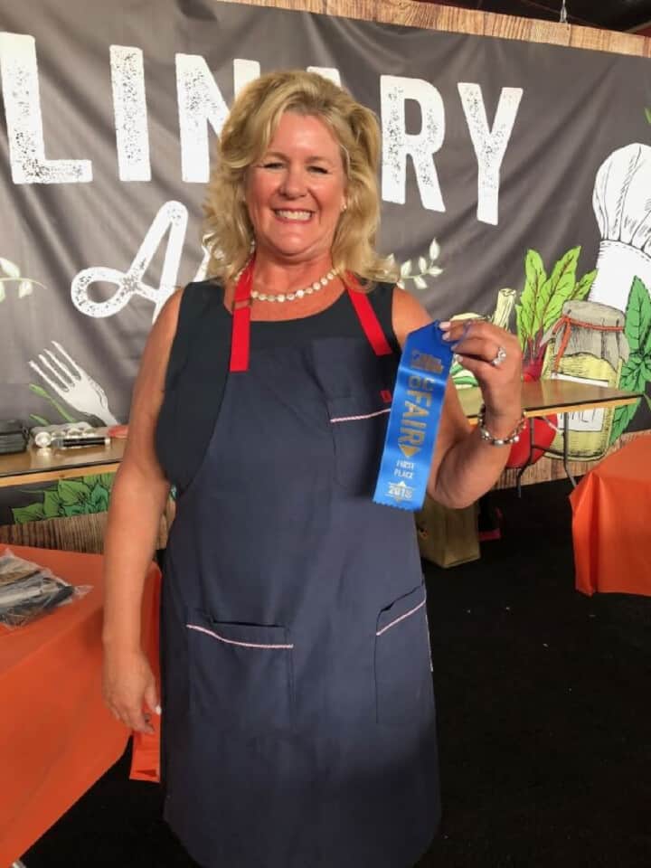 A picture of a lady named Lisa Hatfield holding a blue 1rst place ribbon at the OC Fair for culinary award.