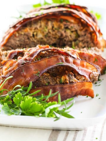 A close up view of meatloaf sliced open and cooked bacon strips on top.