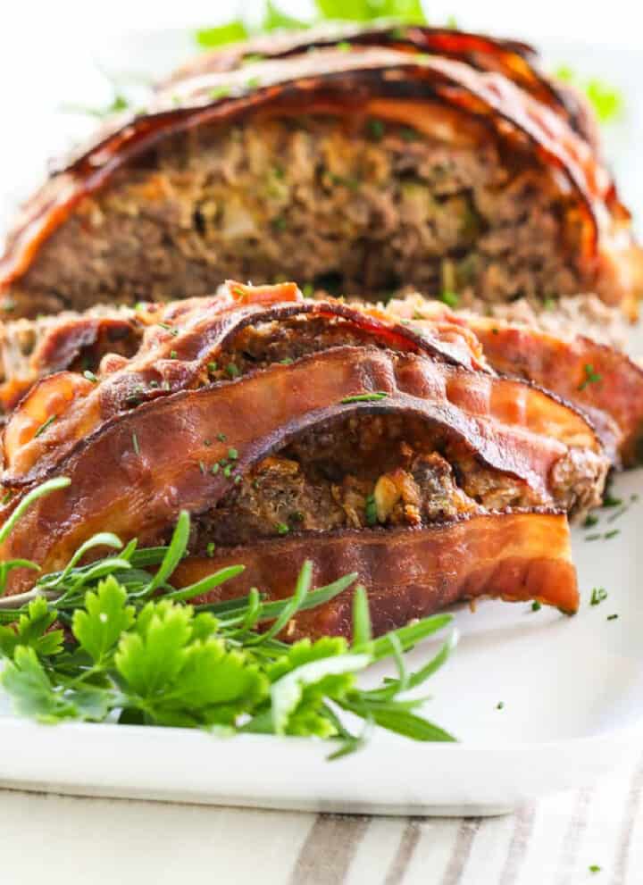 A close up view of meatloaf sliced open and cooked bacon strips on top.