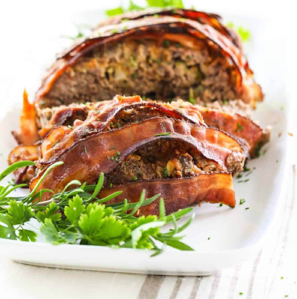 A close up view of meatloaf sliced open and cooked bacon strips on top.
