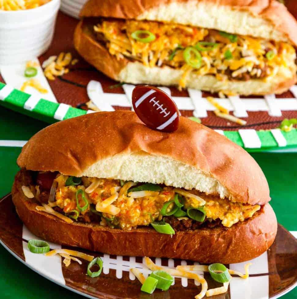 A game day food table with chili dogs loaded with relish, cheese, and onions.