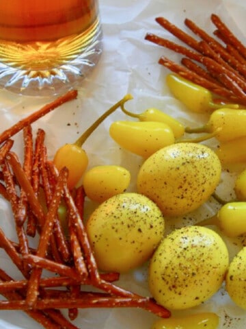 Crinkled parchment paper with a mug of beer, yellow pickled eggs, and pretzel sticks.